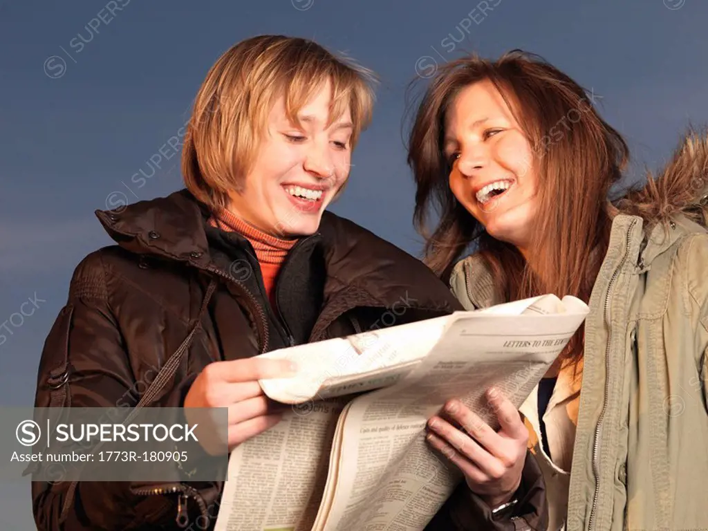 Two women reading newspaper, laughing