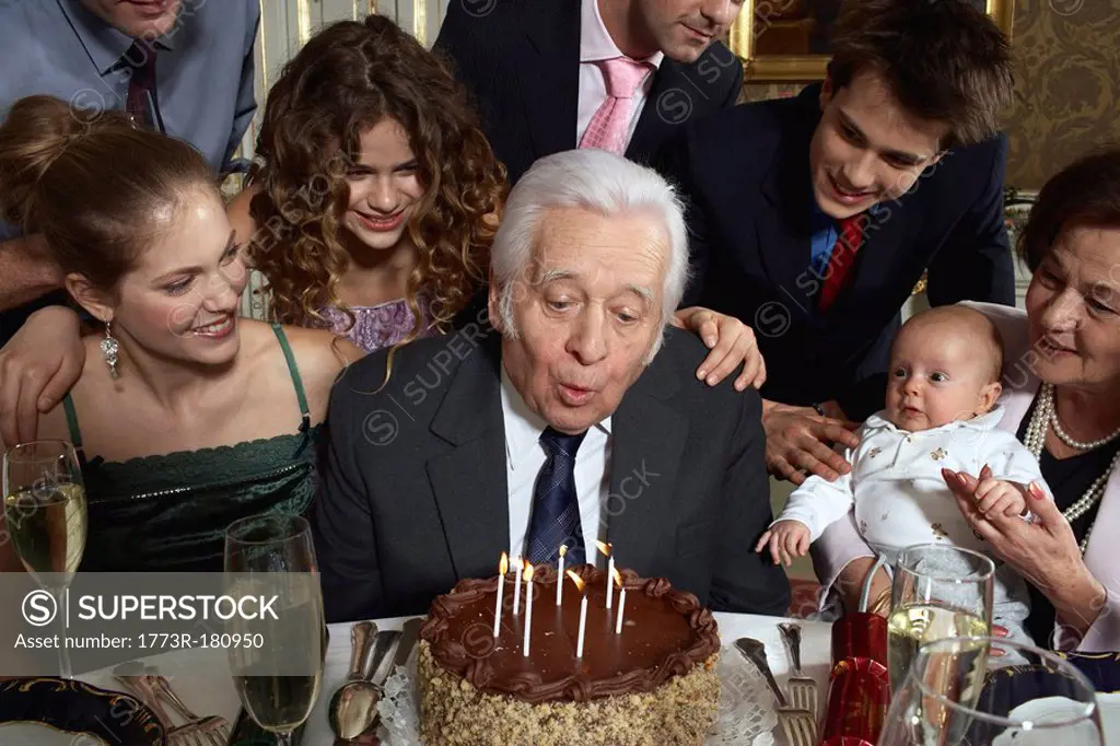 Senior man blowing out candles on cake as family watches