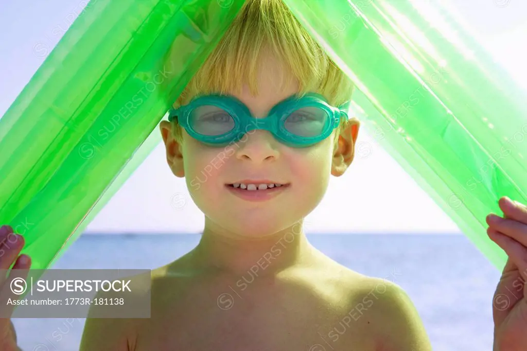 Young boy wearing swim goggles and holding an inflatable raft over his head