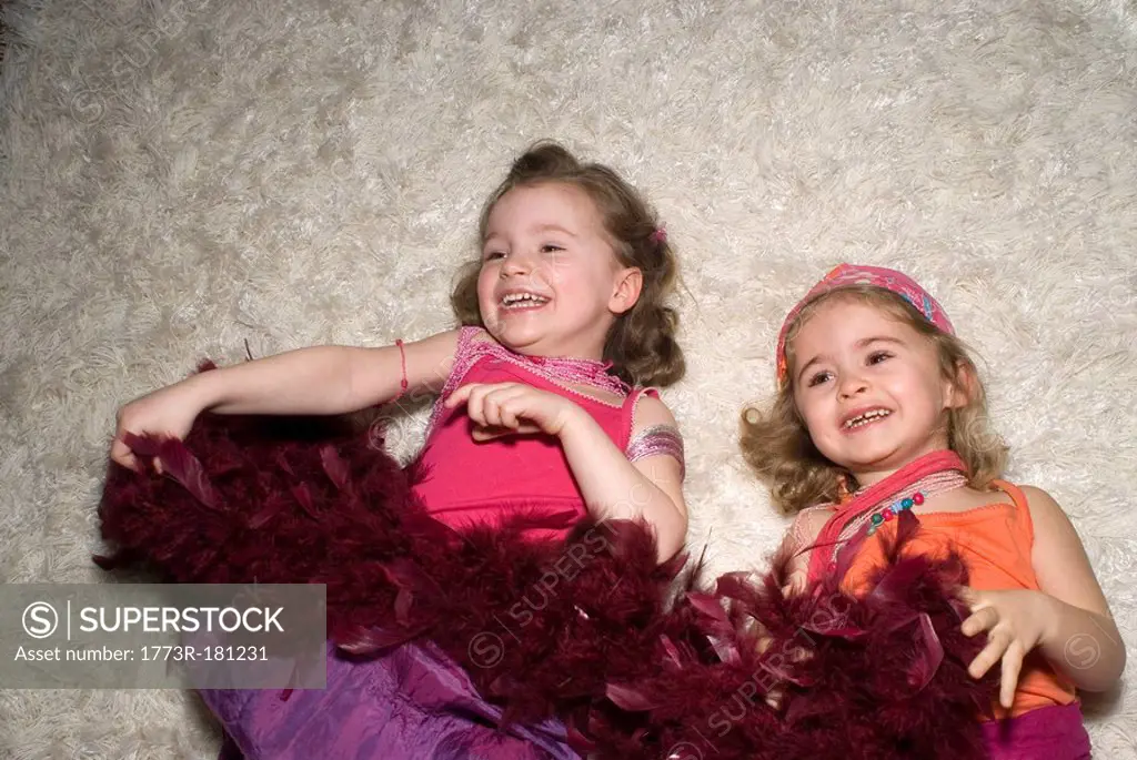 Two girls 2-4 dressed for a party, lying on rug