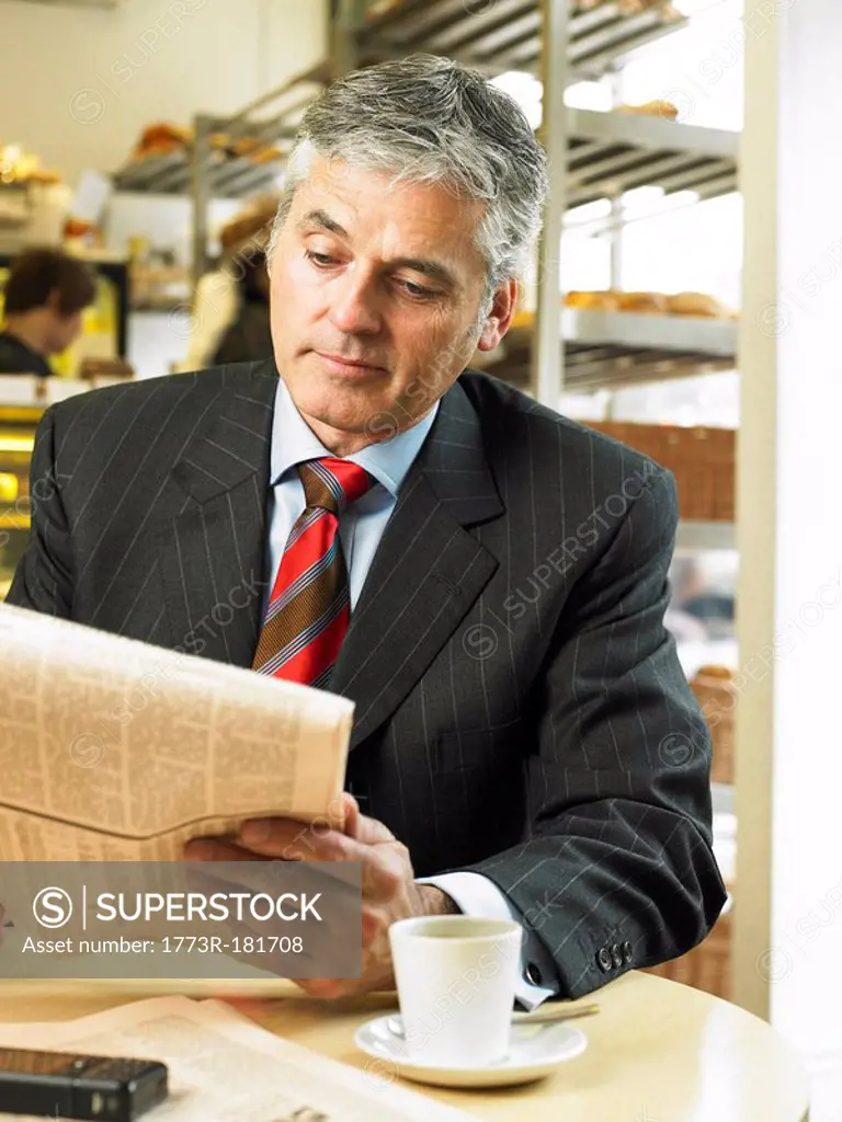 Mature businessman sitting in cafe reading financial newspaper