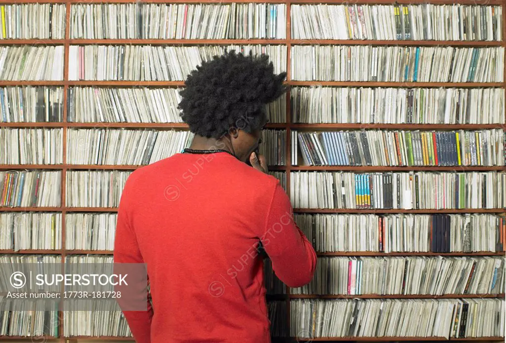 Man looking at compact discs on shelves in music shop, rear view