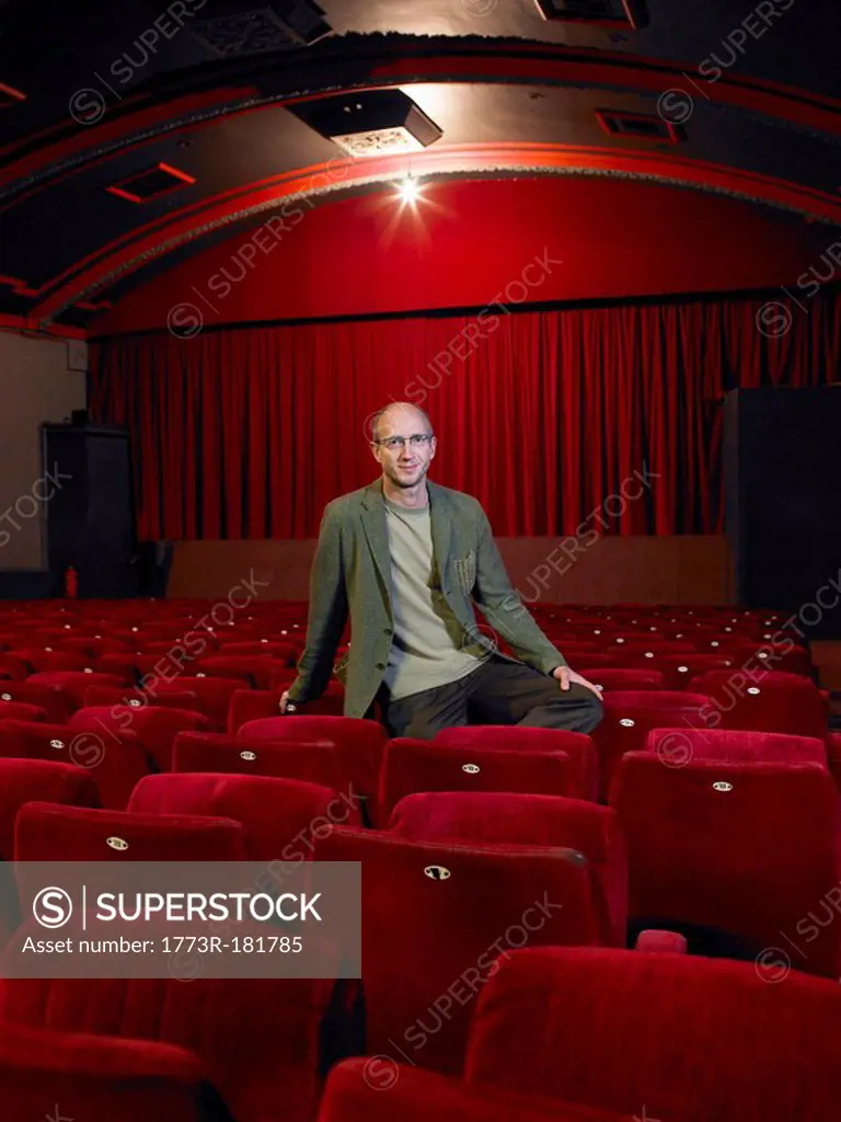 Mature man sitting in empty cinema, smiling, portrait