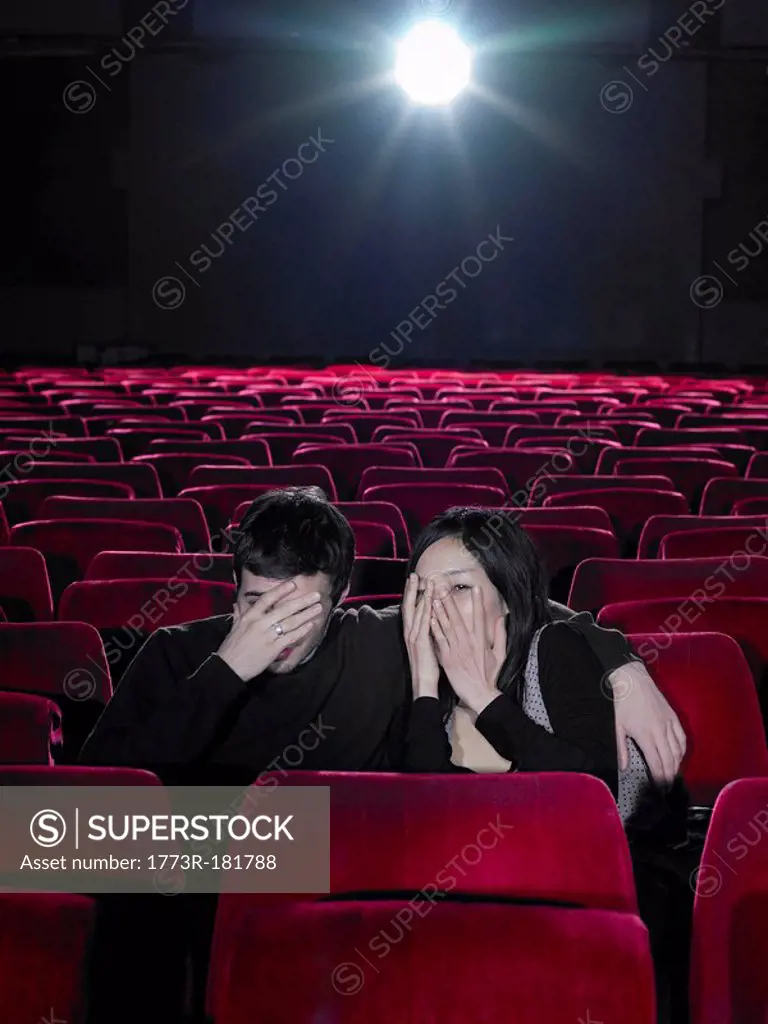 Young couple sitting in cinema holding hands over faces