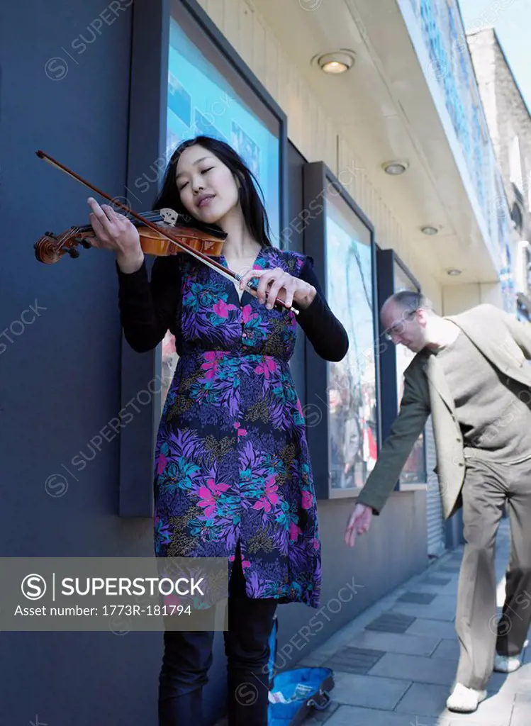 Man giving money to young woman busker playing violin