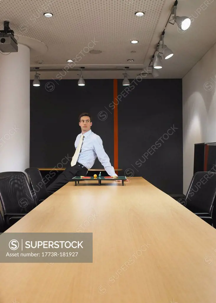 Portrait of young man sitting at boardroom table with miniature table tennis set