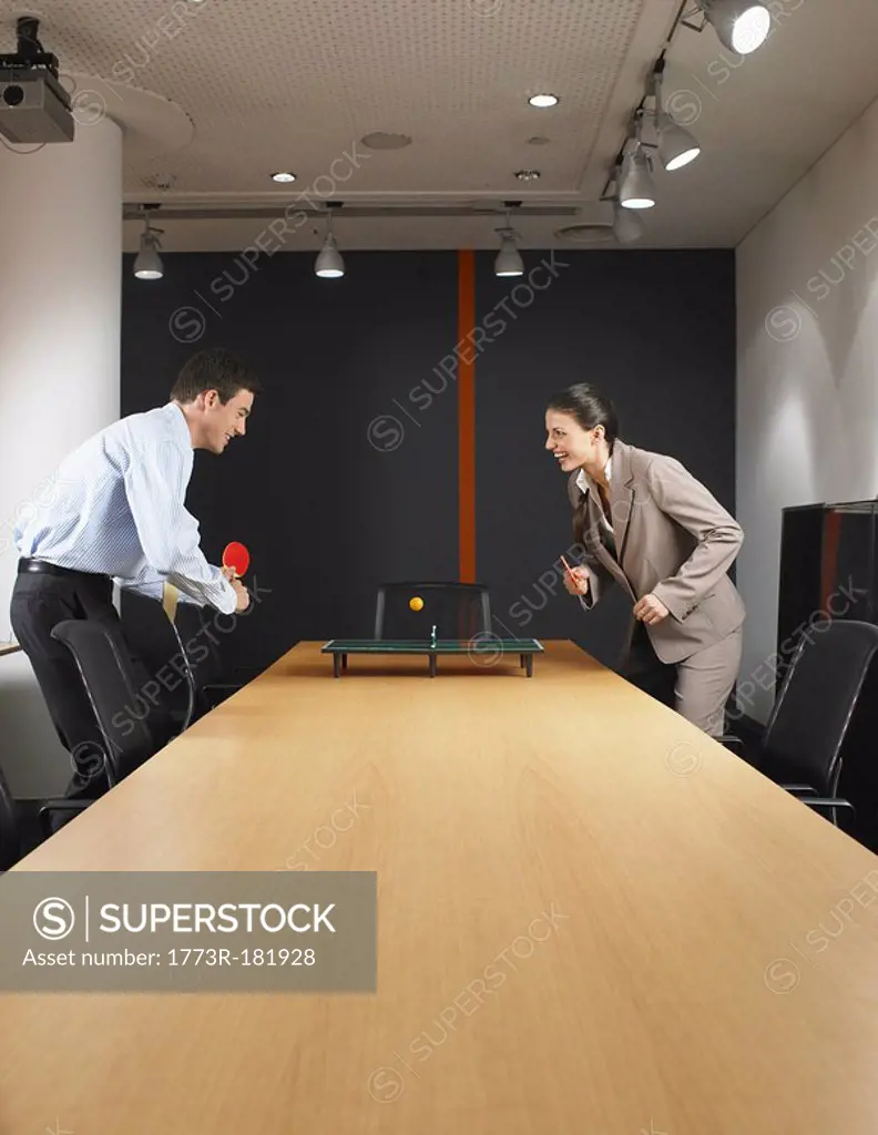 Man and woman playing miniature ping pong at boardroom table