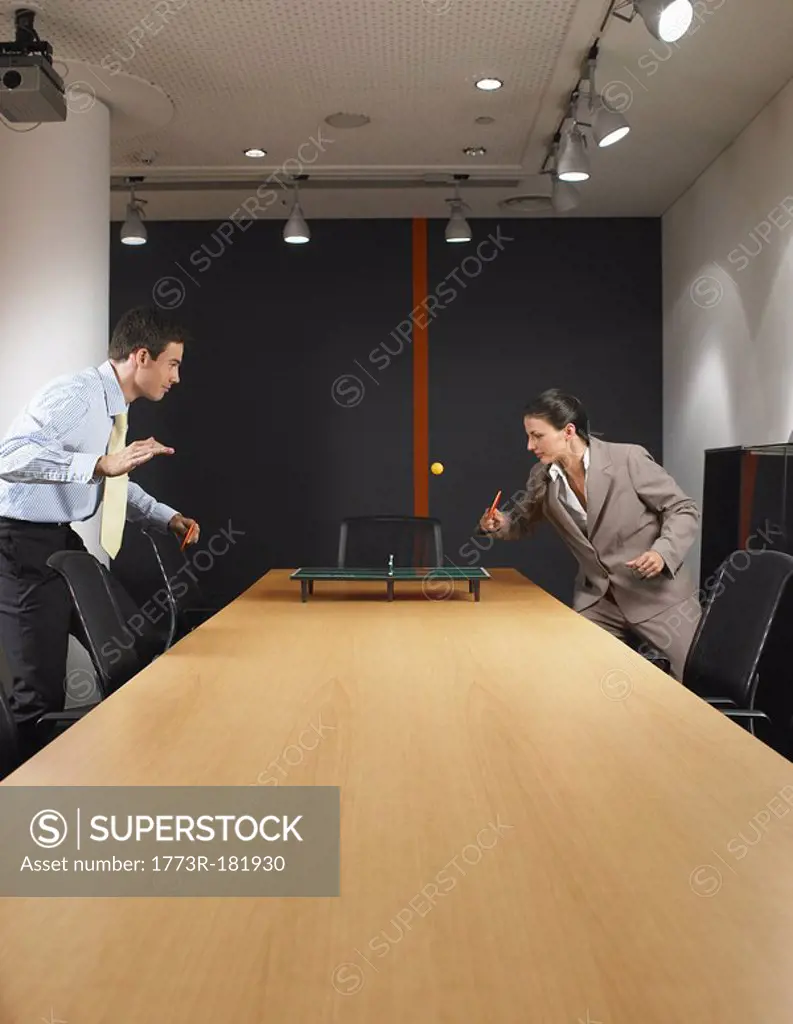 Man and woman playing miniature ping pong at boardroom table