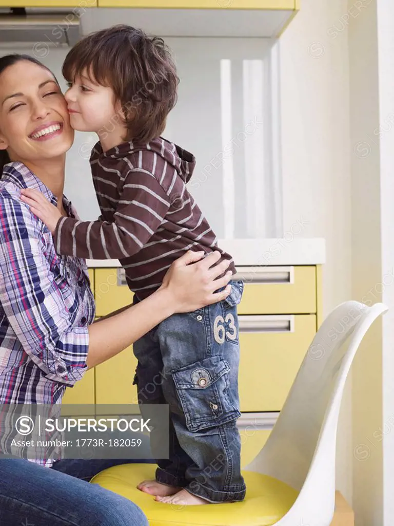 Boy standing on chair kissing mother