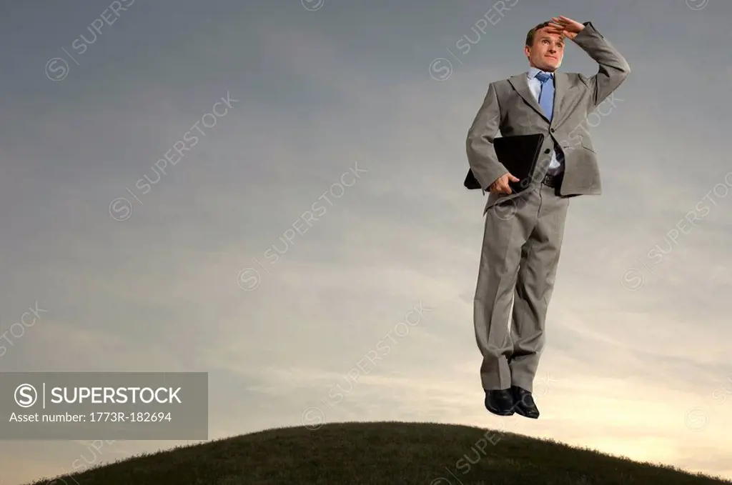 Businessman hovering above hill looking at horizon