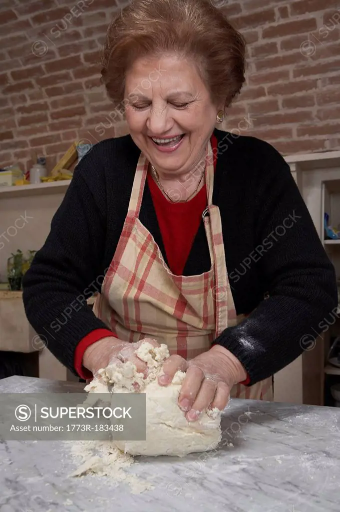 Senior woman kneading dough, smiling