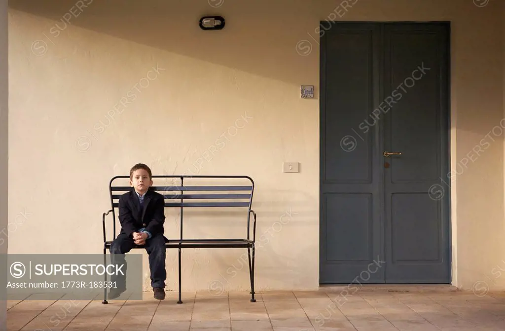 Boy 4-6 sitting on bench outdoors, portrait