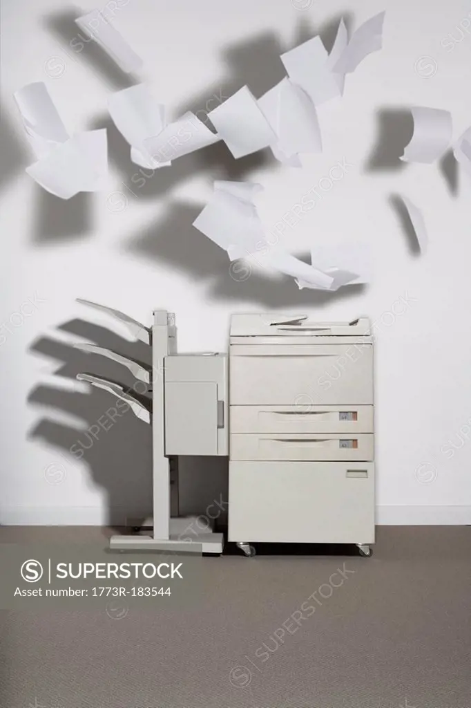 A photocopier against a white wall with paper flying out