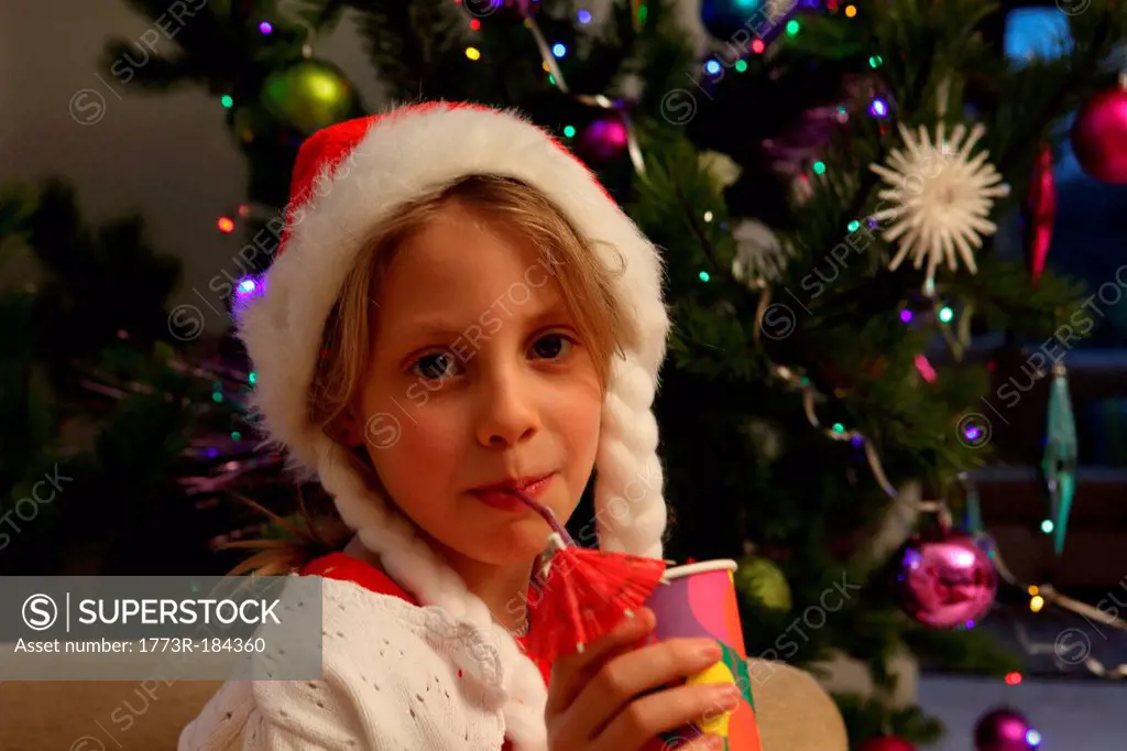 Girl wearing Santa hat by Christmas tree