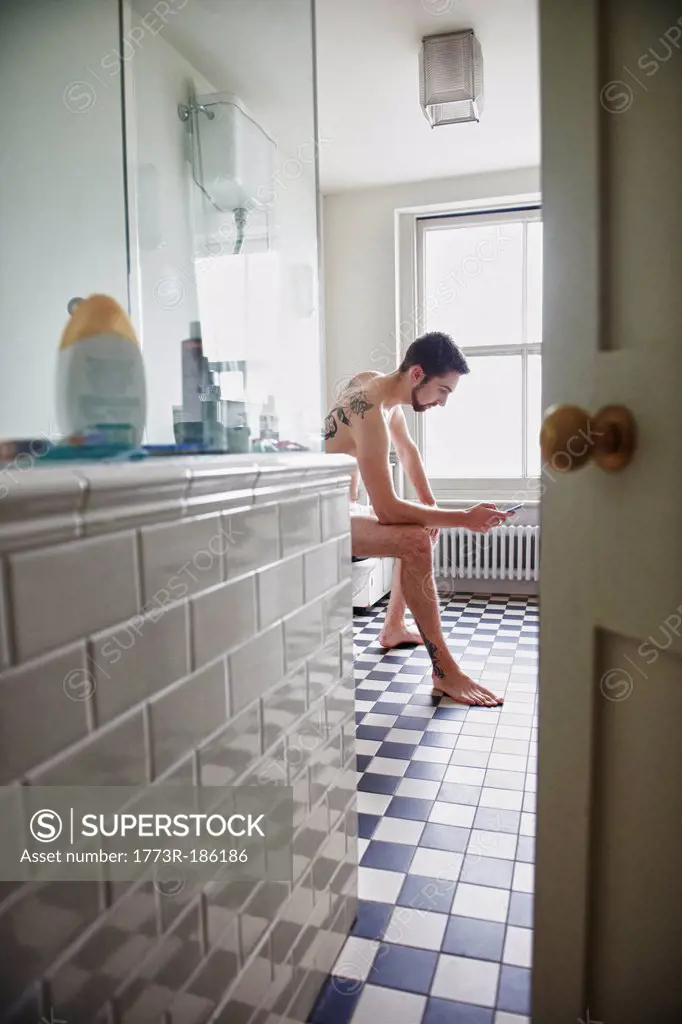 Nude man using cell phone in bathroom