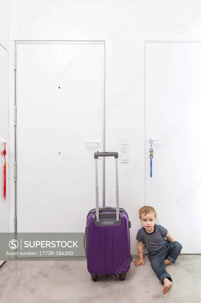 Boy by rolling luggage in hallway