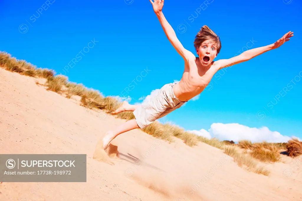 Boy falling on sand dune