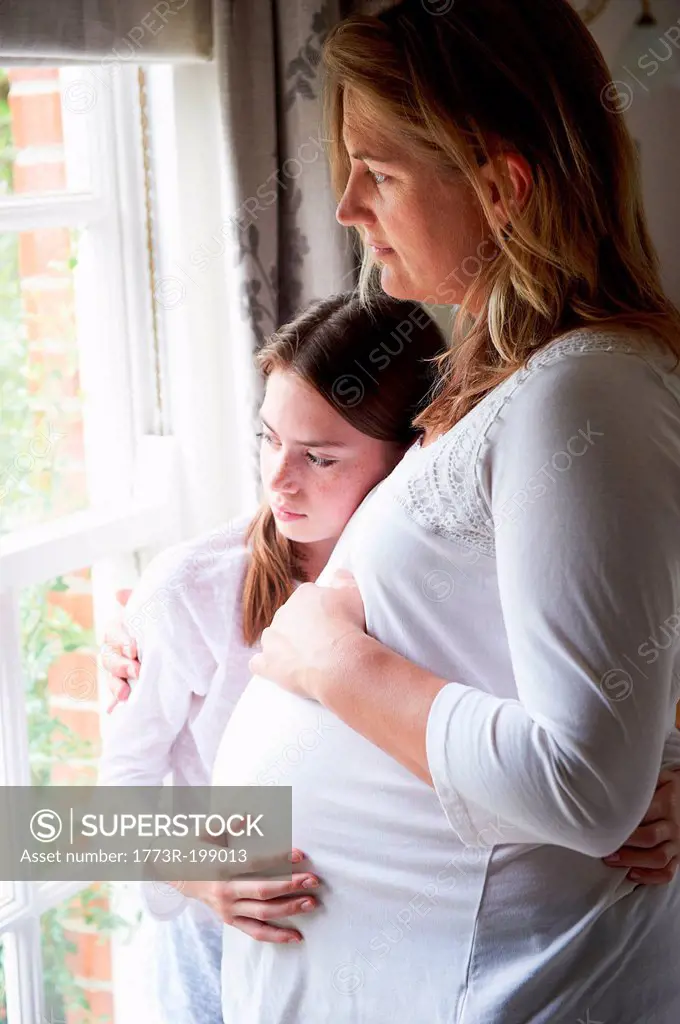 Pregnant mother with teenage daughter looking through window