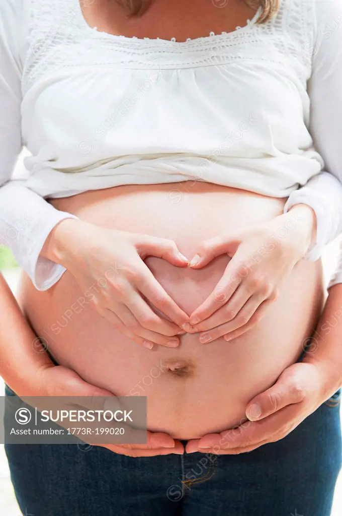Hands in heart shape on pregnant woman's stomach