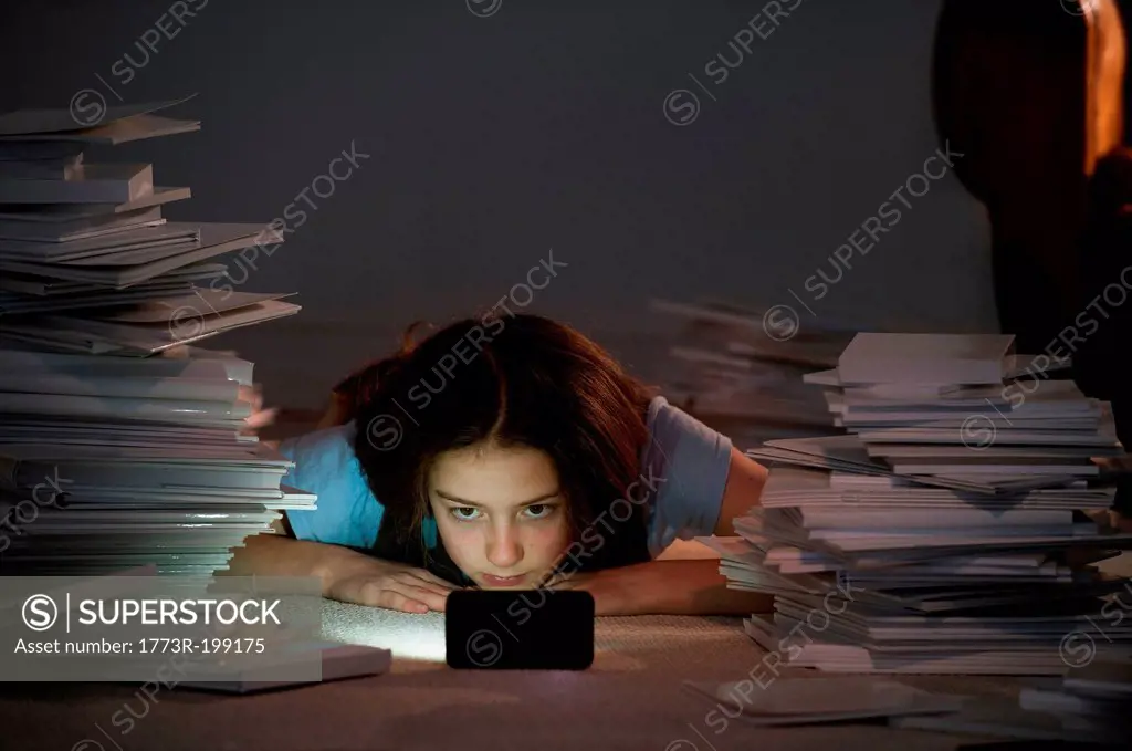 Girl lying on front watching cell smartphone surrounded by books