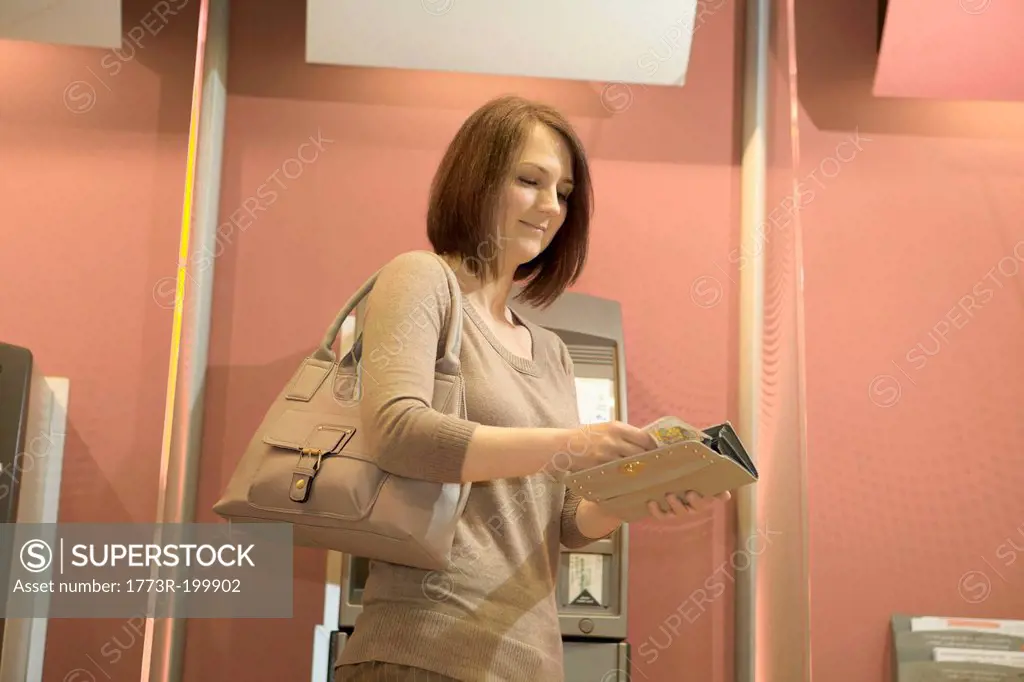 Woman putting banknotes into purse at cashpoint