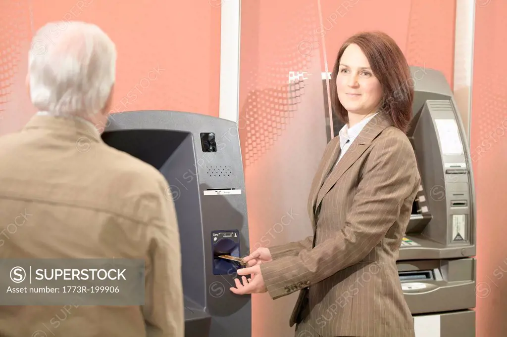 Woman using cashpoint, man waiting