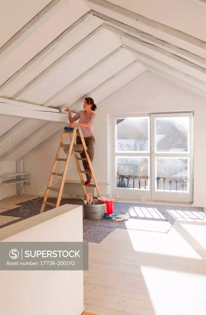 Woman on stepladders painting white ceiling