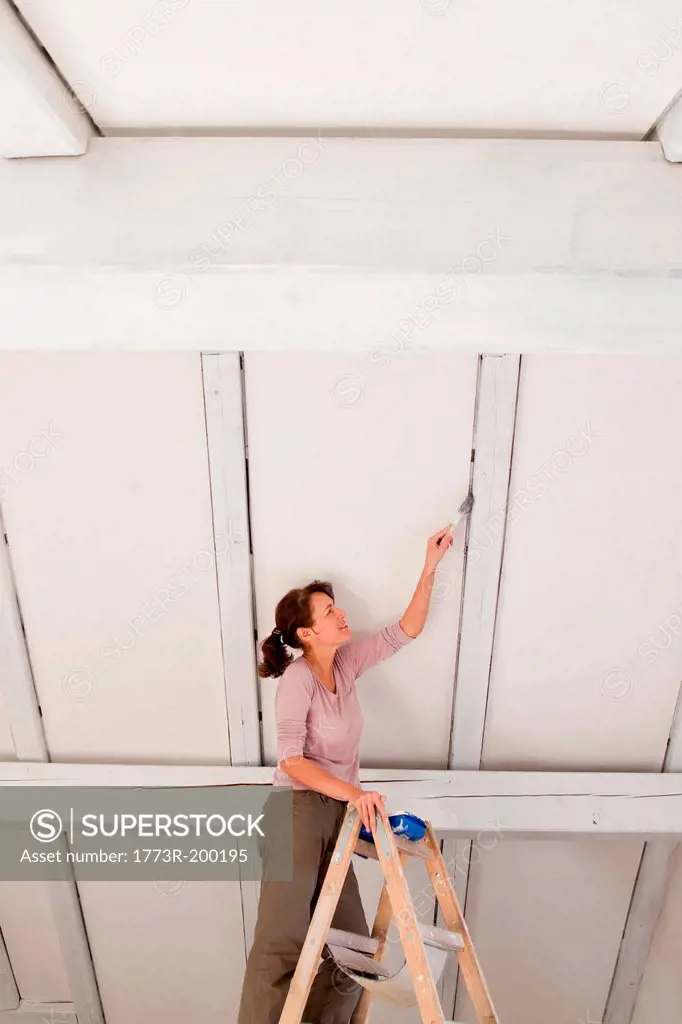 Woman on stepladders painting white ceiling