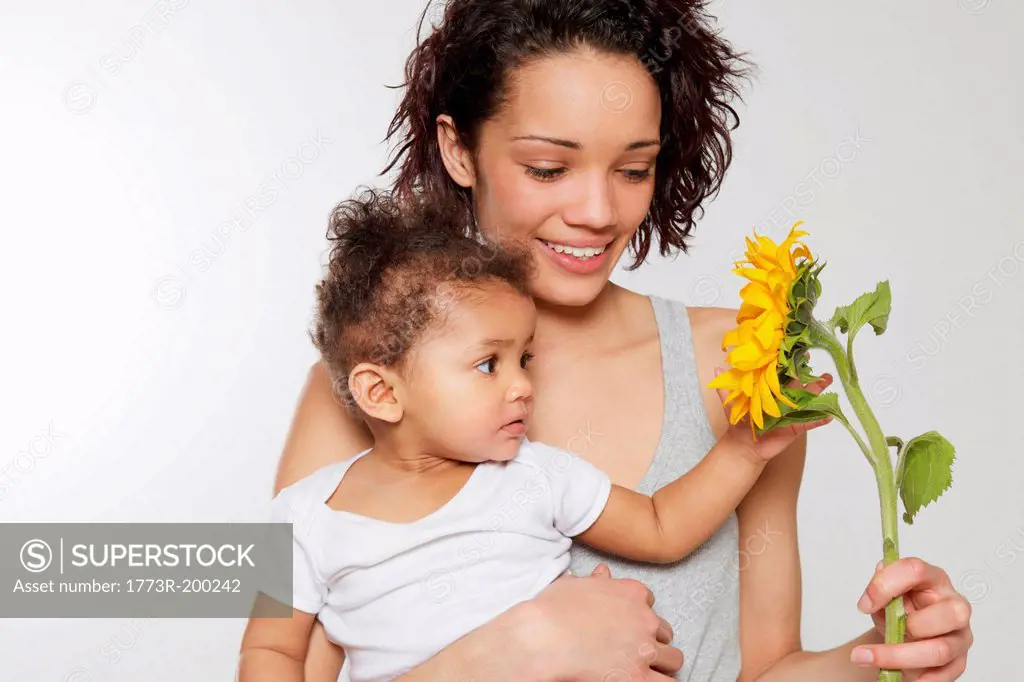 Baby girl touching sunflower held by mother in studio