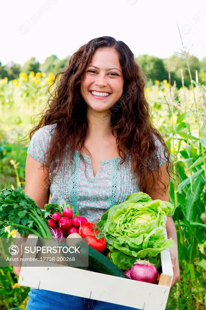 Portrait of young woman holding box of fresh vegetables in allotment