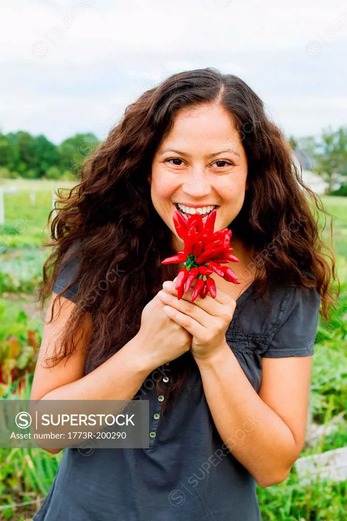 Portrait of young woman holding crop of red chillies in allotment