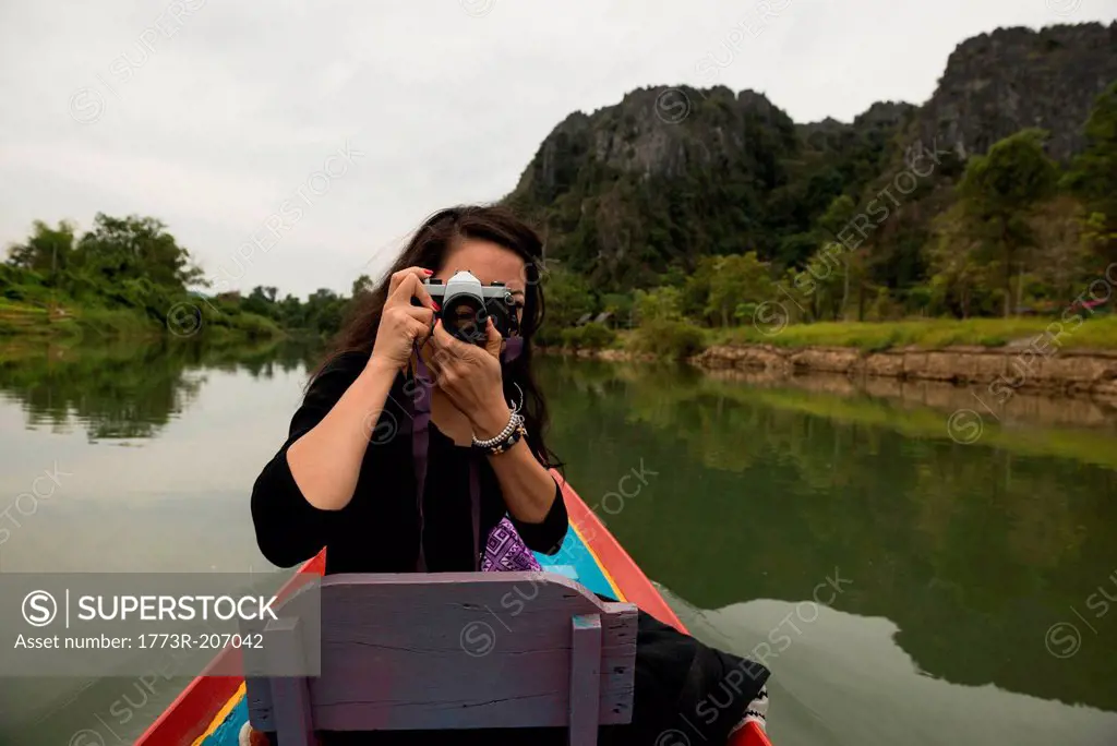 Woman taking photograph on boat on Nam Song River, Vang Vieng, Laos