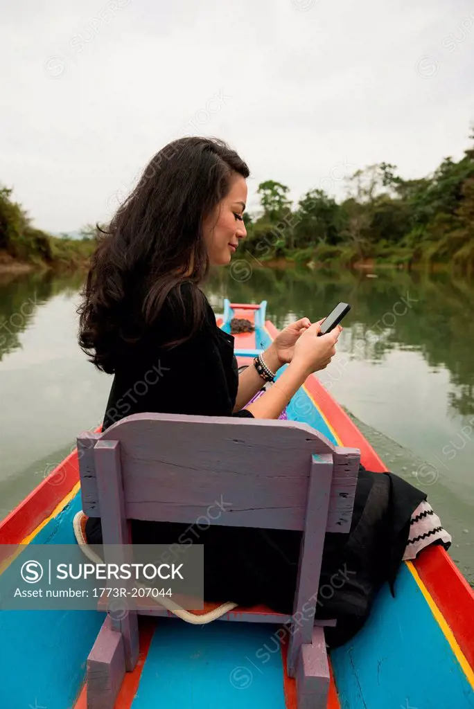 Woman with mobile phone on boat on Nam Song River, Vang Vieng, Laos