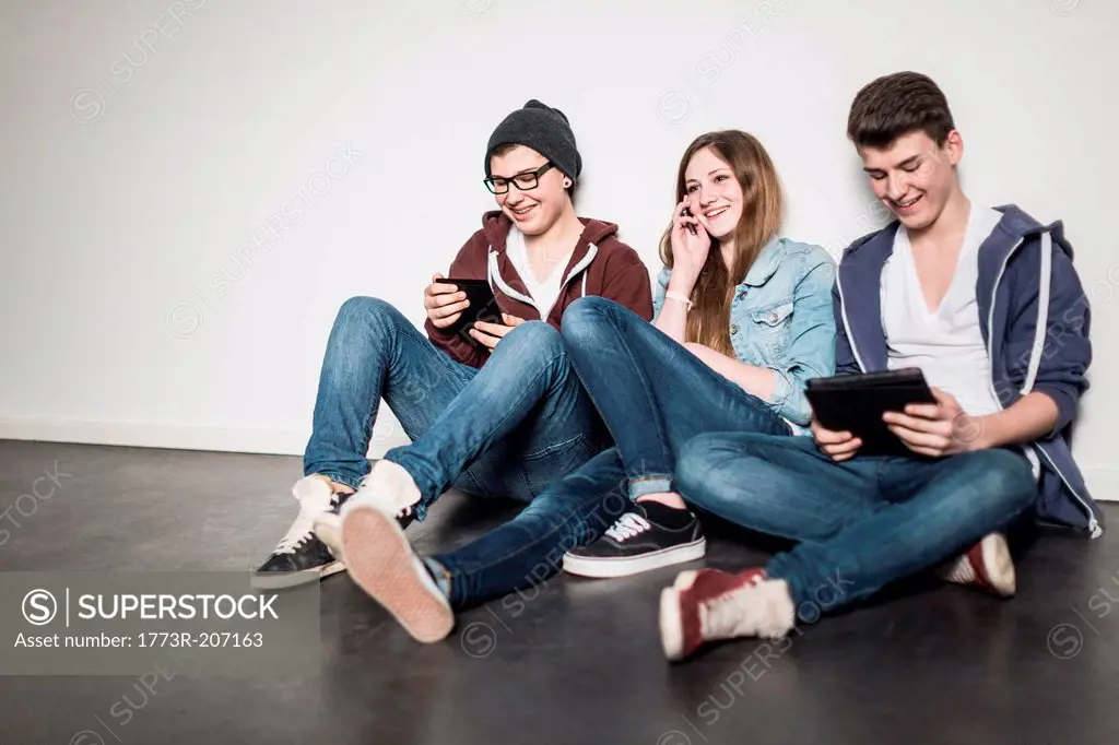Three teenagers sitting on floor using technology