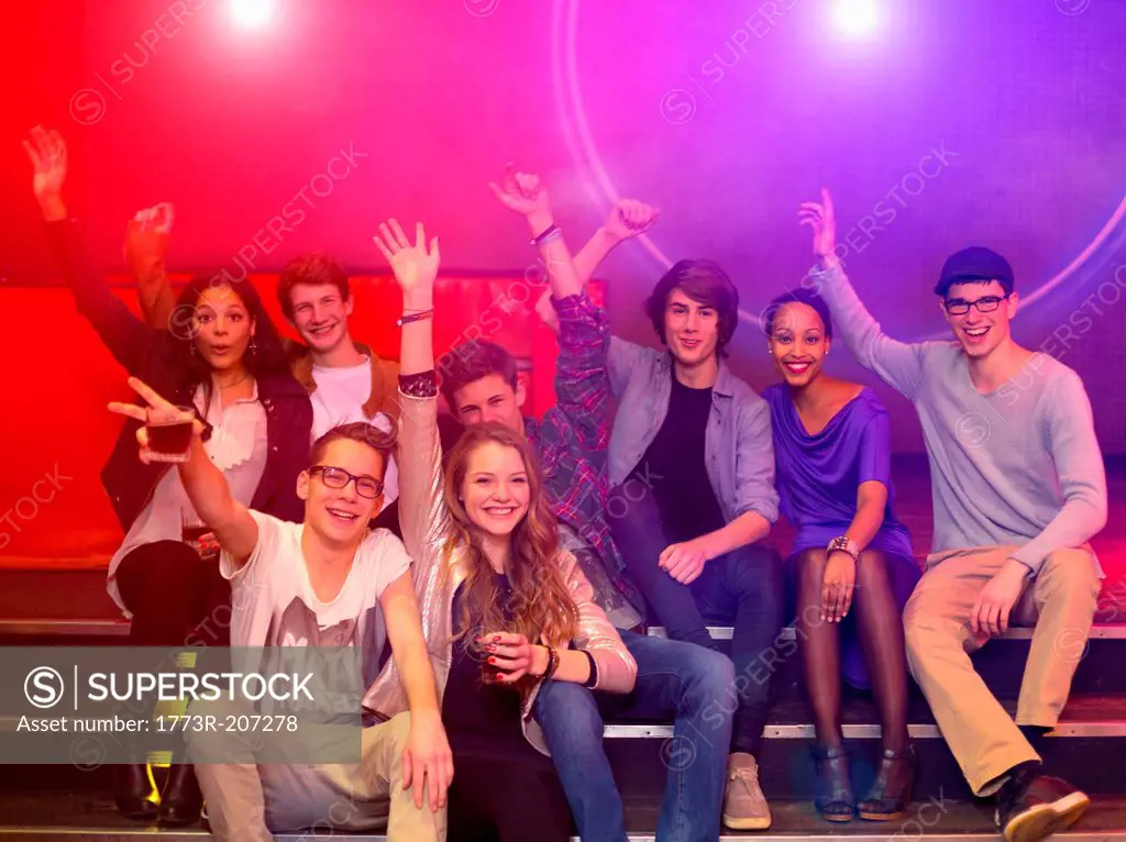 Group of teenagers and young adults at party holding drinks and raising arms