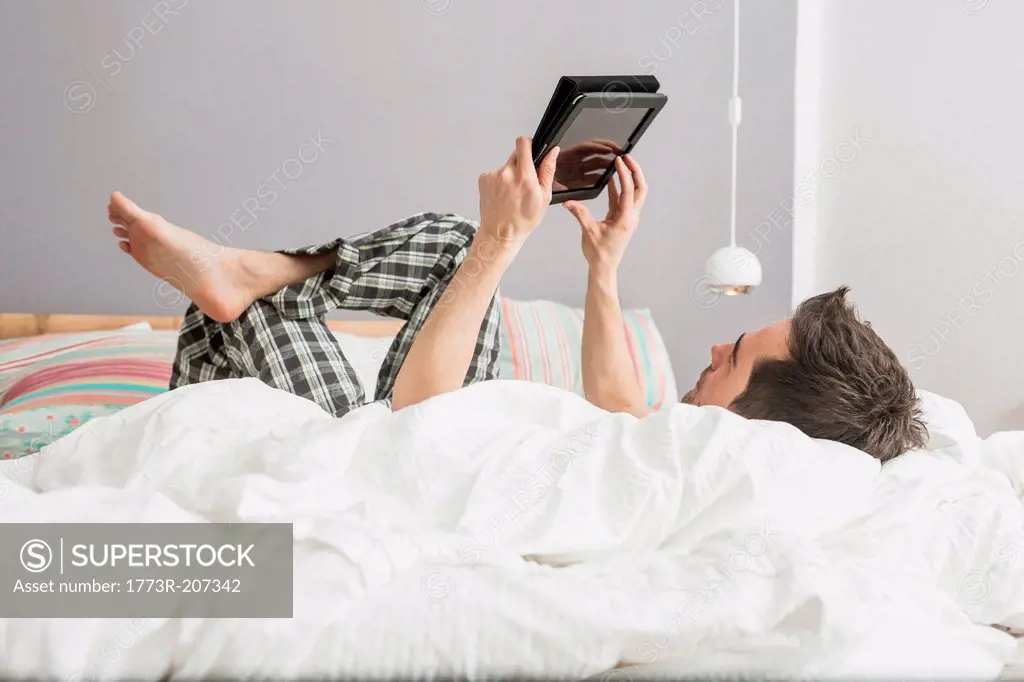 Mid adult man lying on bed using digital tablet