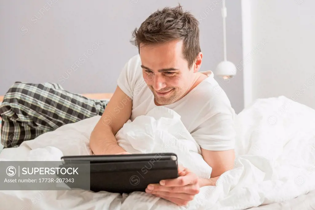 Mid adult man lying on bed using digital tablet