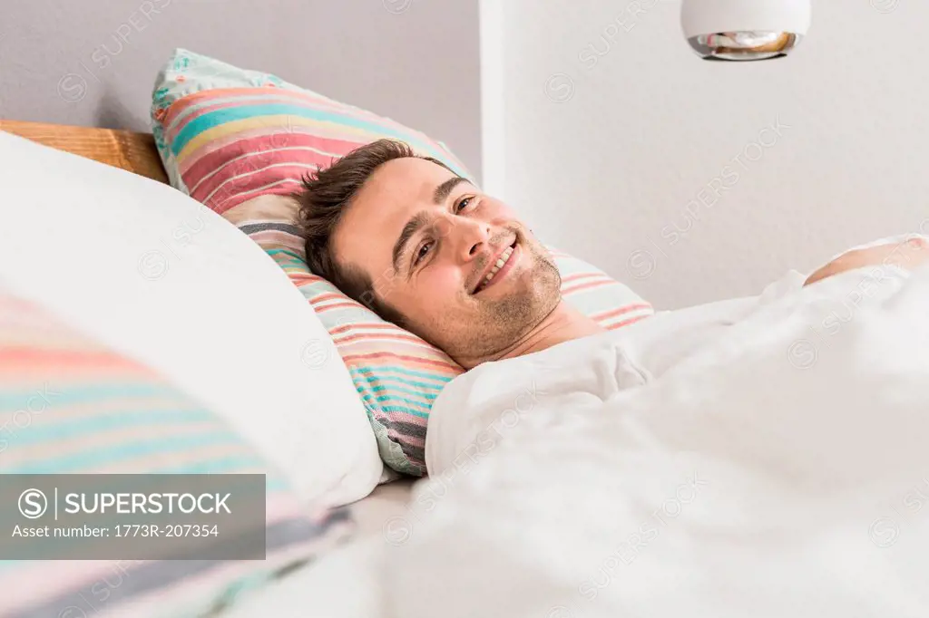 Mid adult man lying in bed under duvet