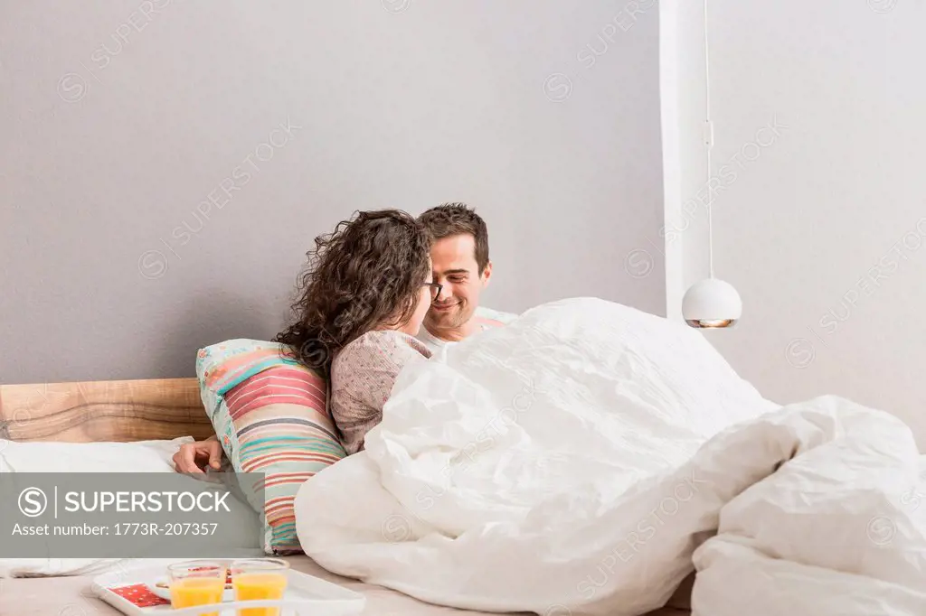 Mid adult couple lying in bed, breakfast on tray