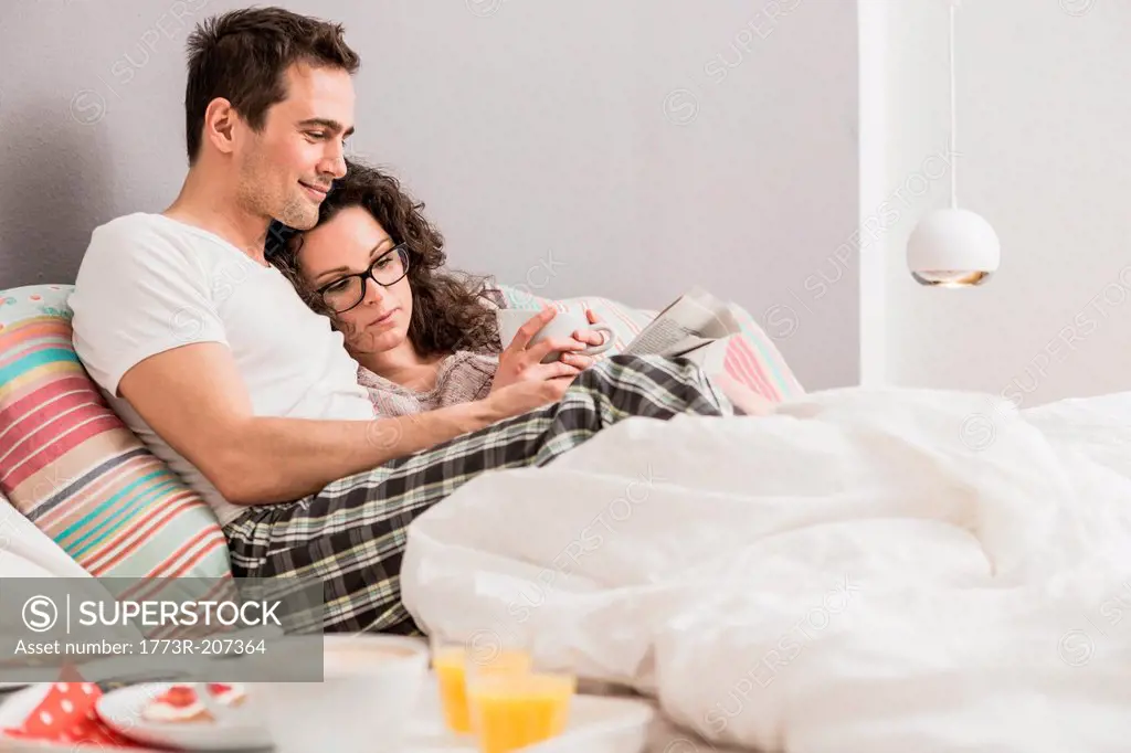 Mid adult couple reading newspaper in bed