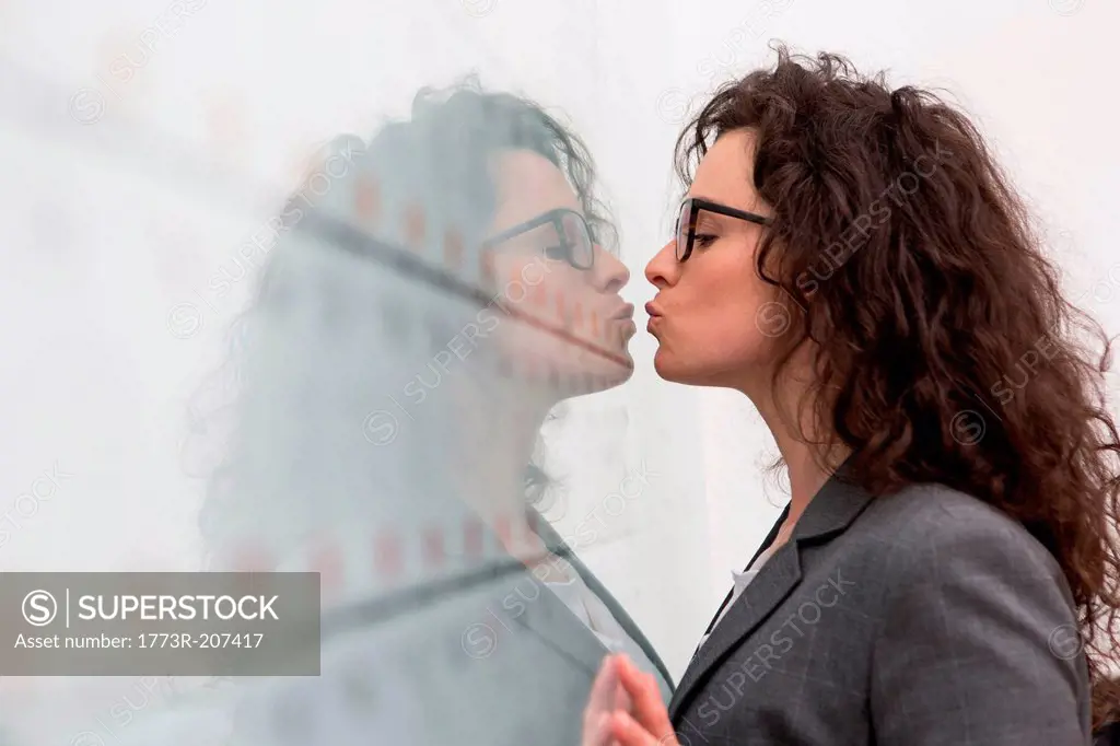 Businesswoman kissing her reflection on wall