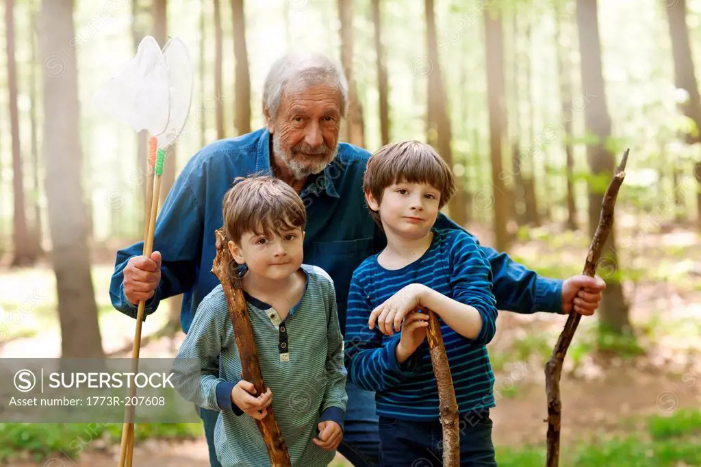 Grandfather and grandsons holding sticks in forest, portrait