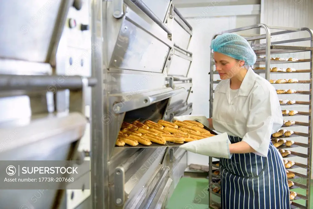 Baker removing tray of baked pastries from oven in bakery