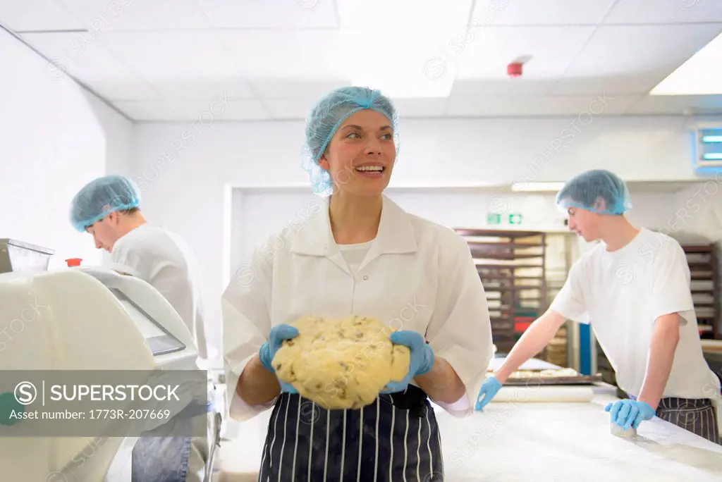 Baker holding dough as staff work behind
