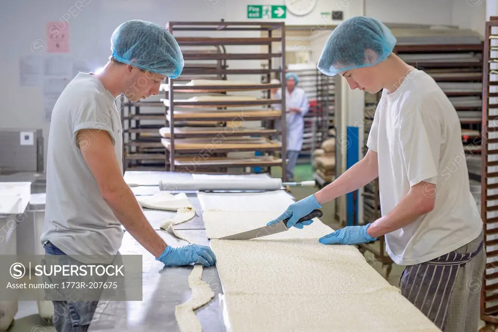Bakers in protective clothing preparing length of dough