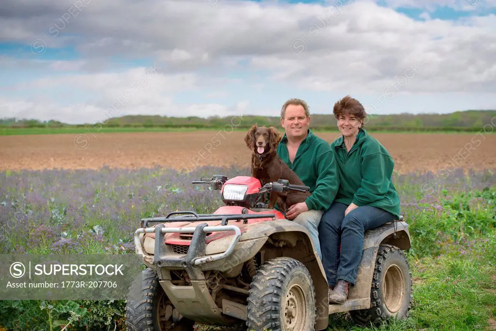 Farmer, wife and pet dog on quad bike in field of organic farm