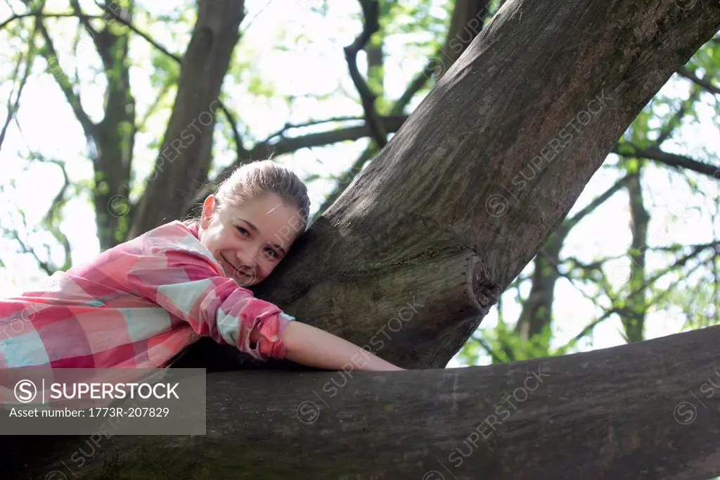 Portrait of young girl lying on top of tree branch