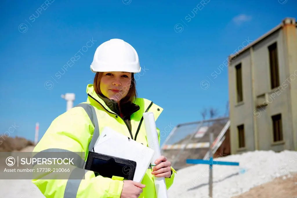 Portrait of female with blueprint and digital tablet on construction site