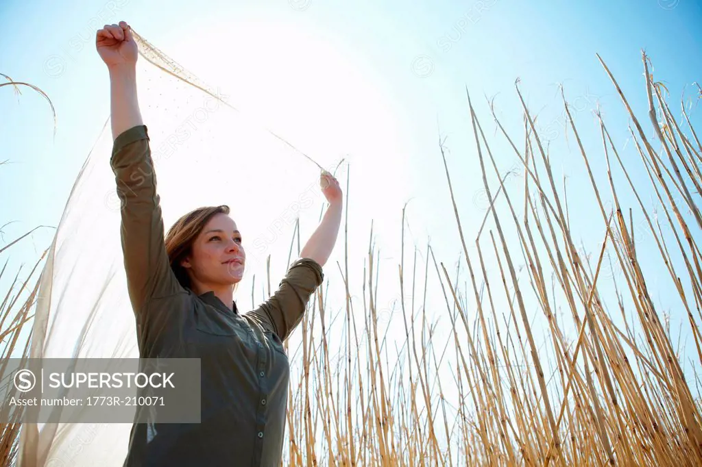 Young woman holding up scarf in reeds