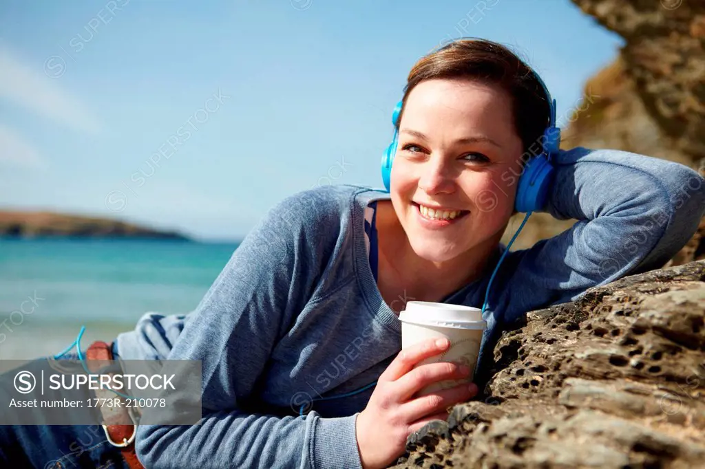 Portrait of young woman at coast with coffee and earphones